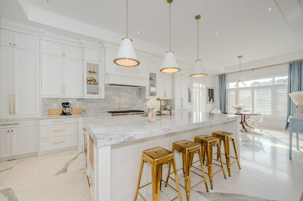 A kitchen with white cabinets , marble counter tops , and gold stools.