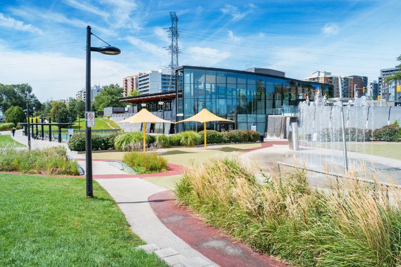 A park with a fountain and umbrellas in front of a building.
