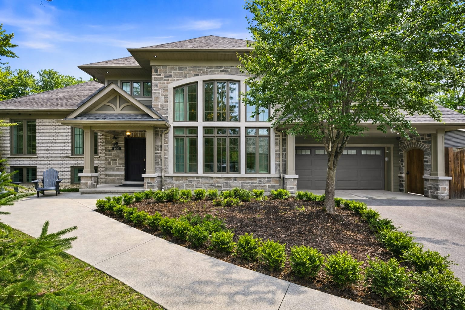 Stone and brick custom home with tall arched windows, a gabled front porch and a double garage behind a landscaped front bed.