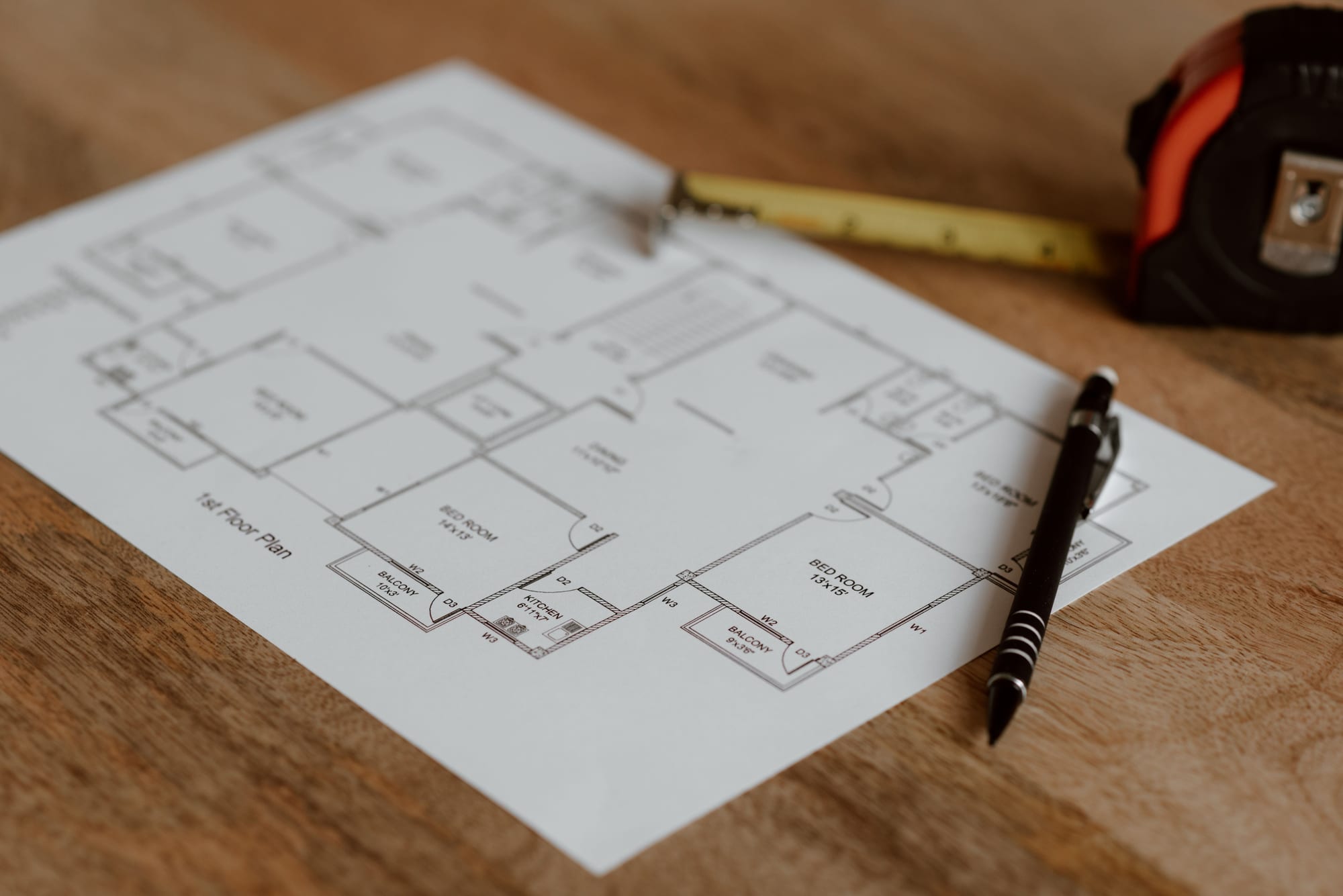 First-floor architectural plan on a wooden table with a pen and a tape measure.