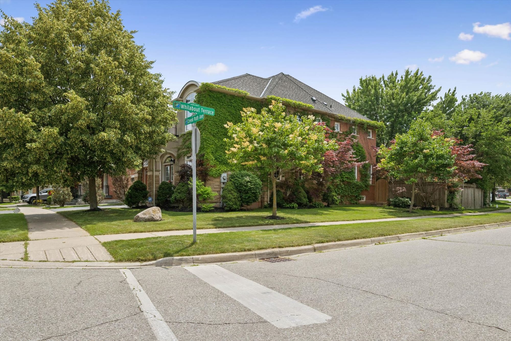 Ivy-covered brick home on a corner lot, with street signs at the intersection, mature trees and a wide lawn.