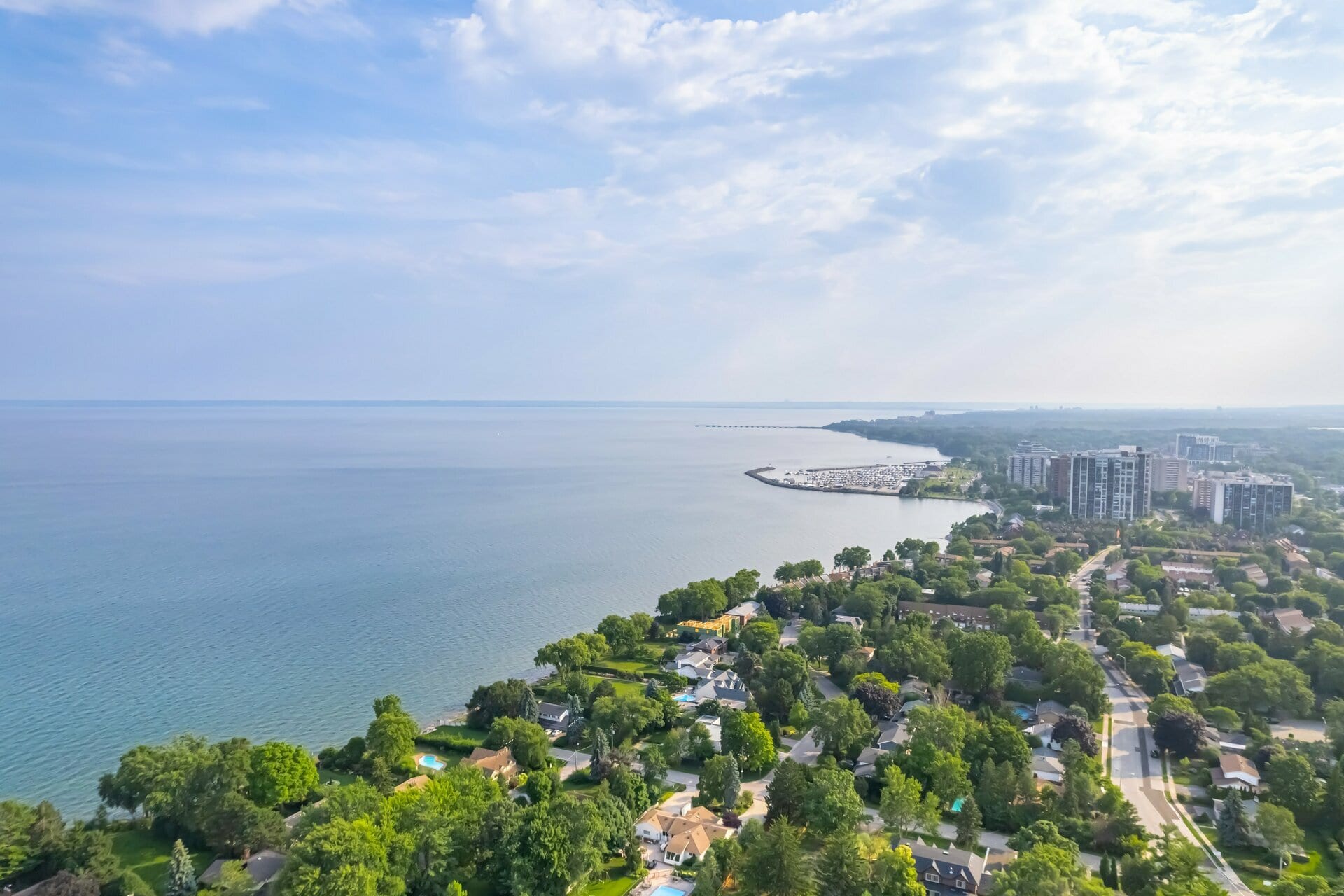 Aerial view of a tree-lined Lake Ontario shoreline with waterfront homes, a harbour and condominium towers.