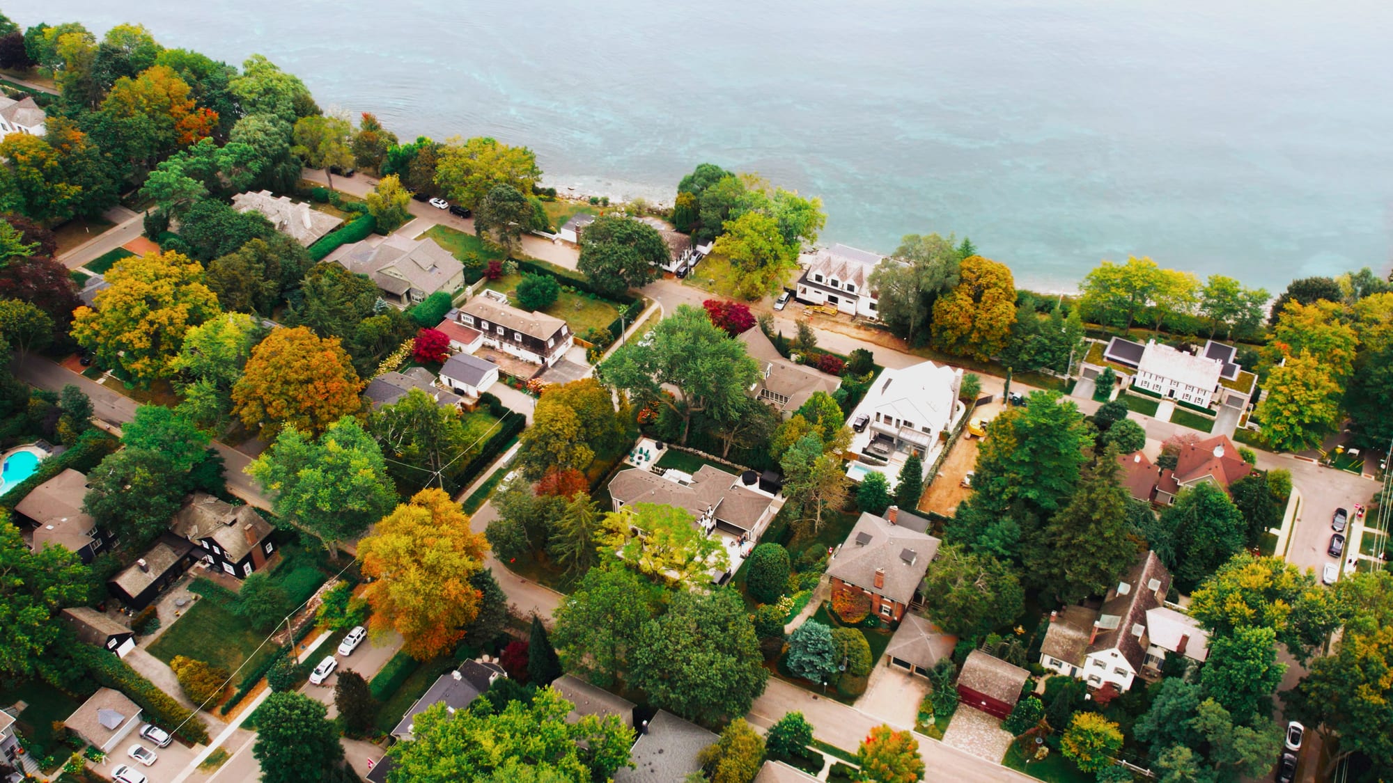 Aerial view of lakefront homes among autumn trees along the Lake Ontario shoreline.