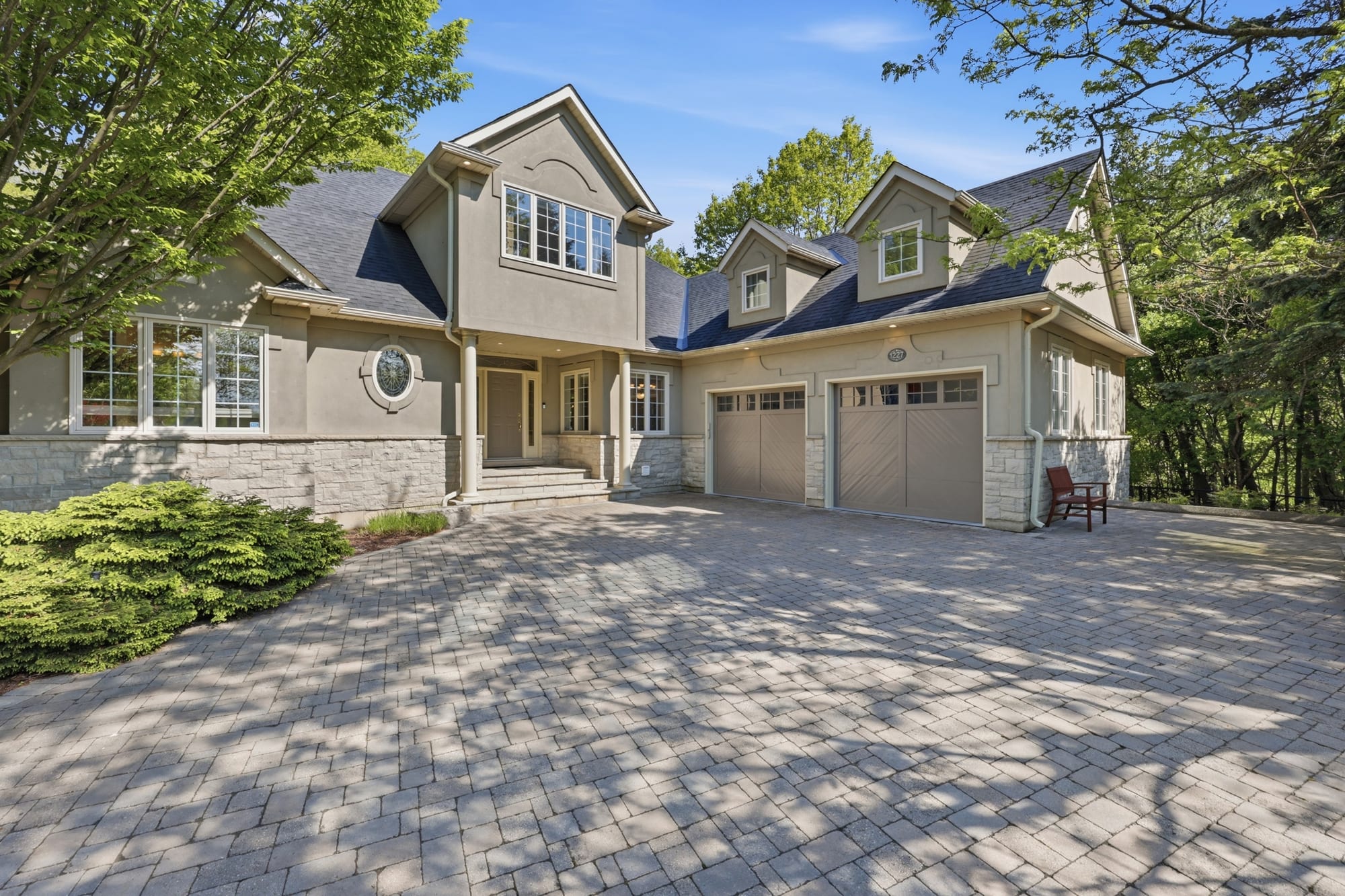Stucco-and-stone home with an interlock driveway among mature trees in Oakville, marketed by the Dan Cooper Group.