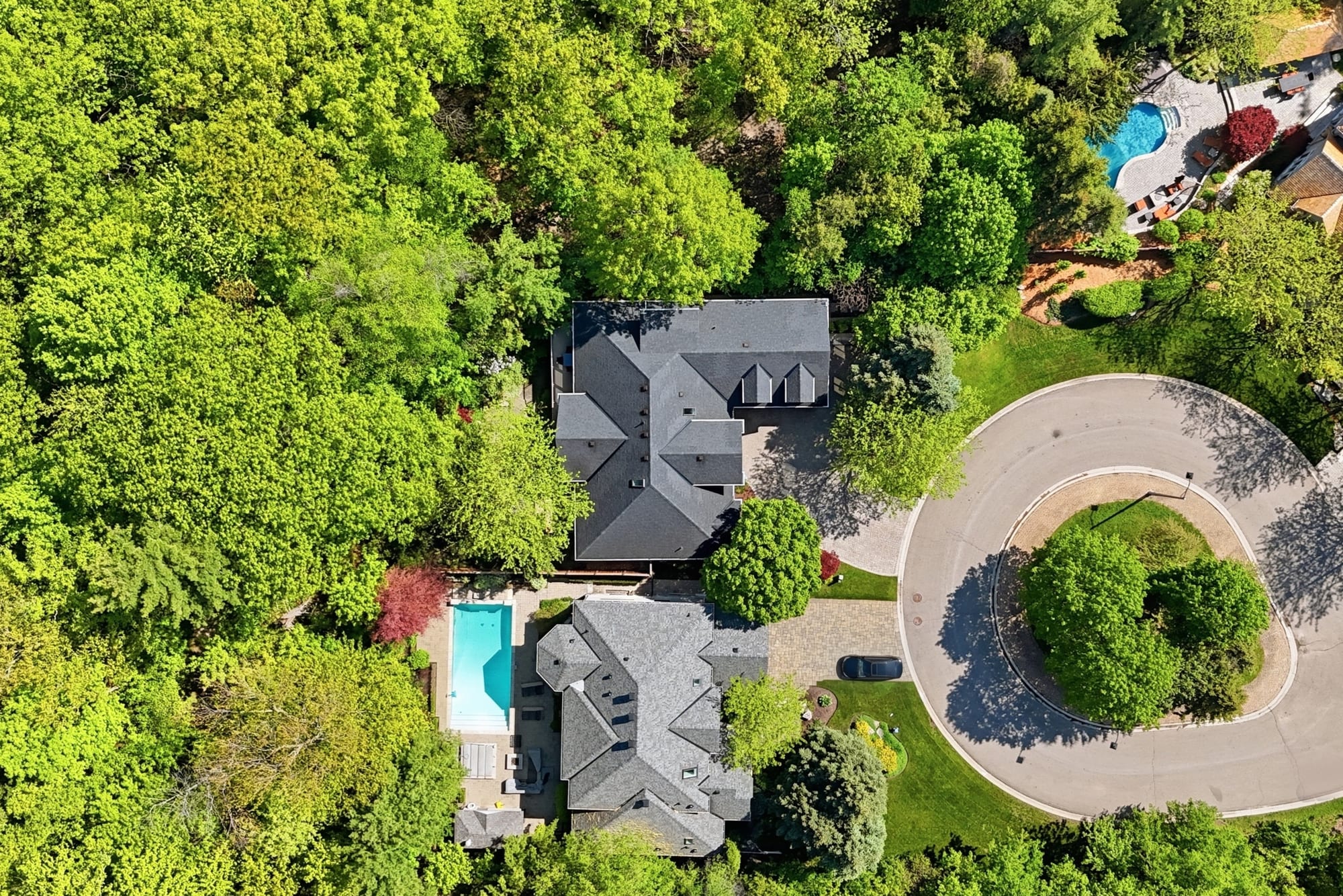 Aerial view of two large homes on a wooded ravine lot at the end of a cul-de-sac, one with a backyard pool, surrounded by mature trees.