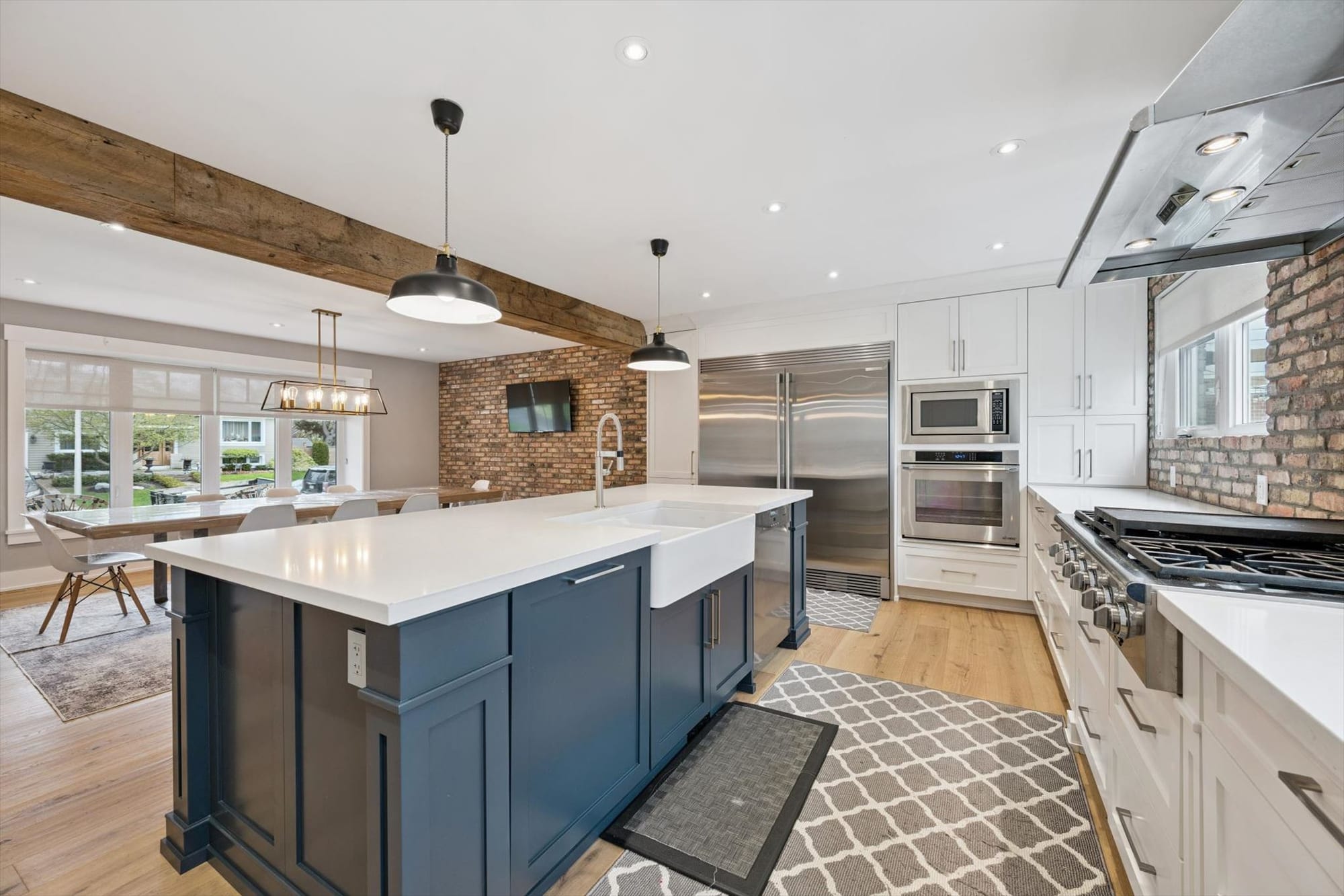 Renovated kitchen with a navy island, white shaker cabinets, exposed brick and a reclaimed wood beam.