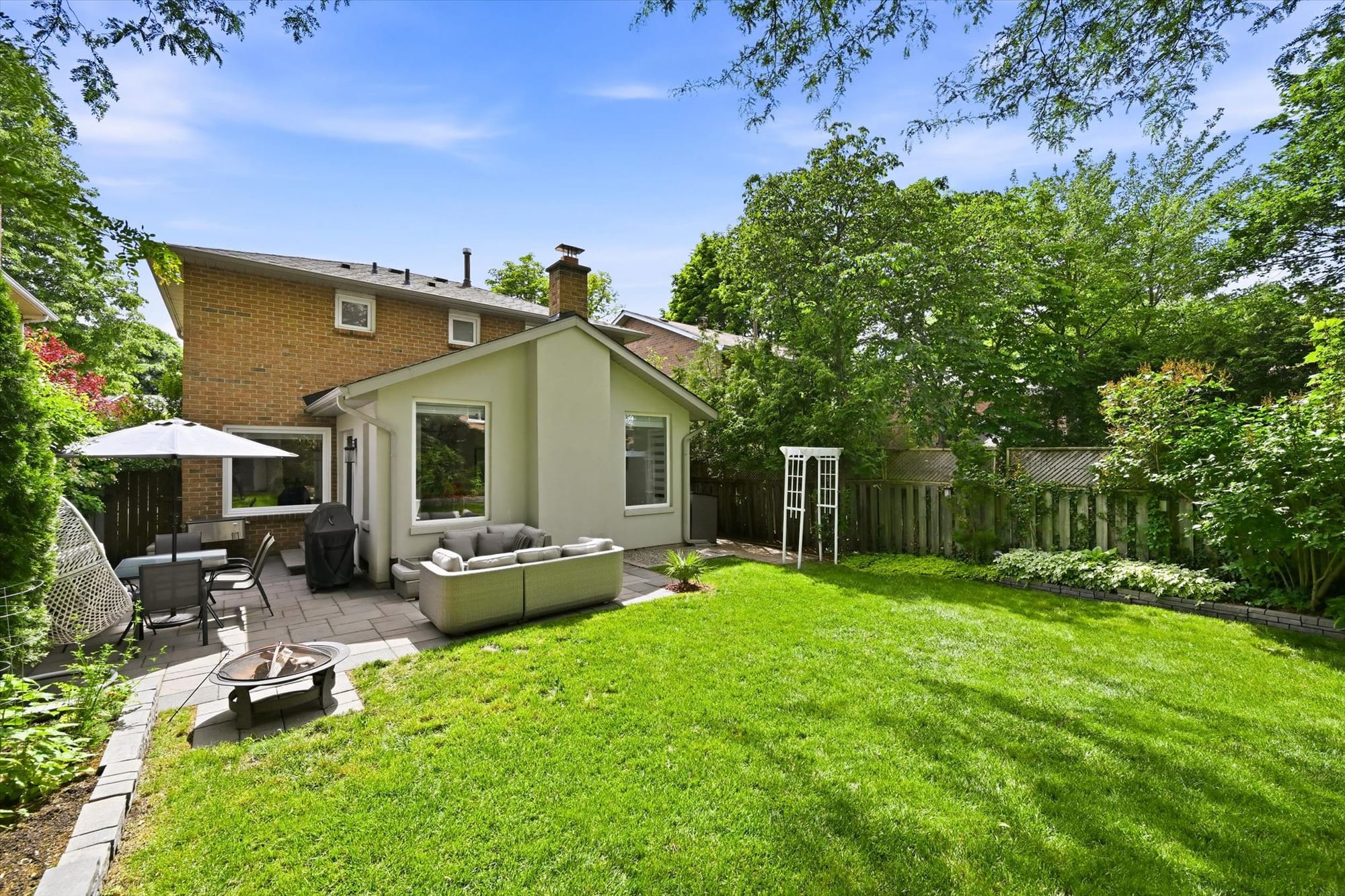 Private, tree-lined backyard with a stone patio and lounge seating at an Oakville home, marketed by the Dan Cooper Group.