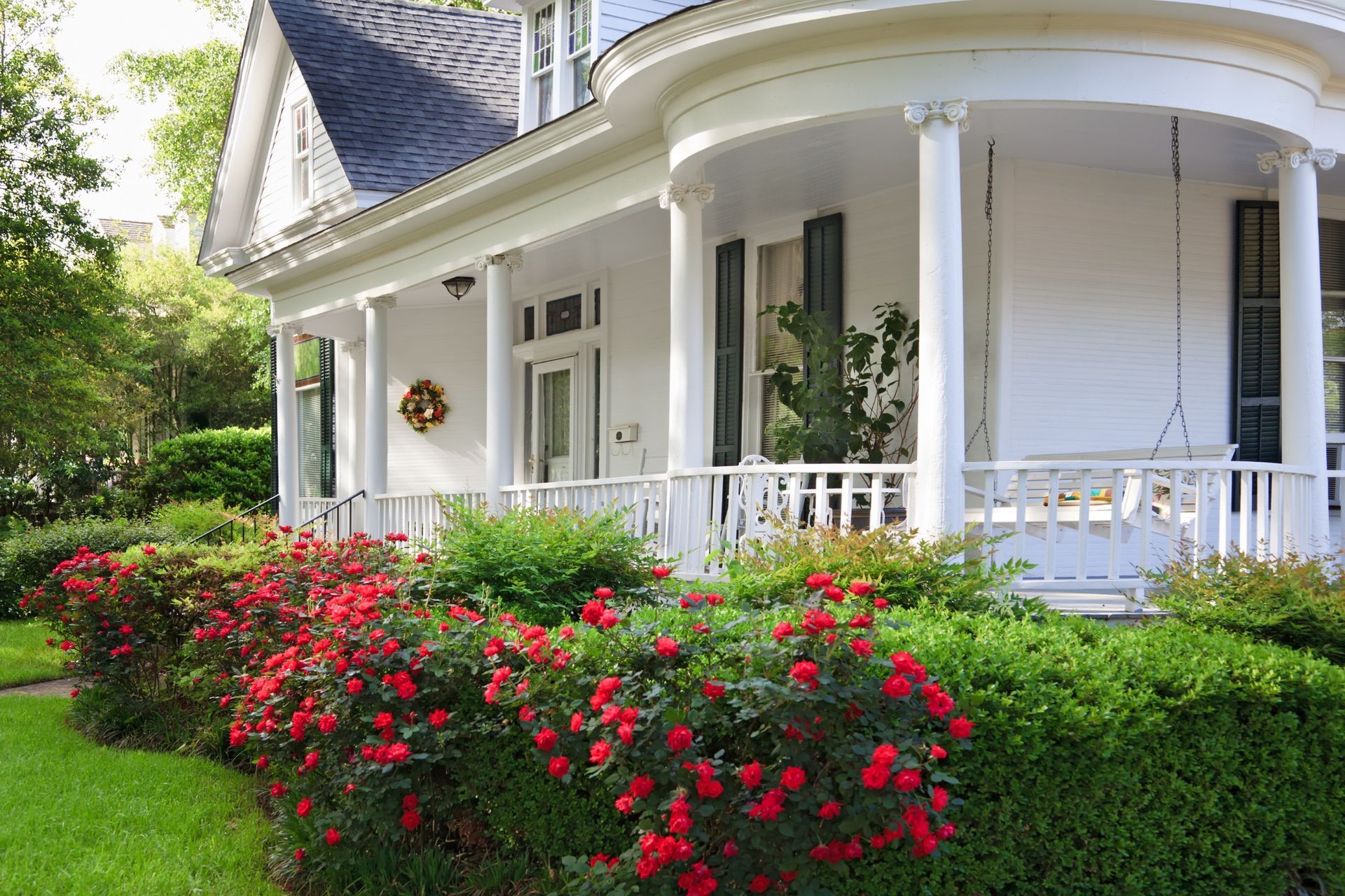 Exterior photo of a white home with a wrap around porch and beautiful landscaping.