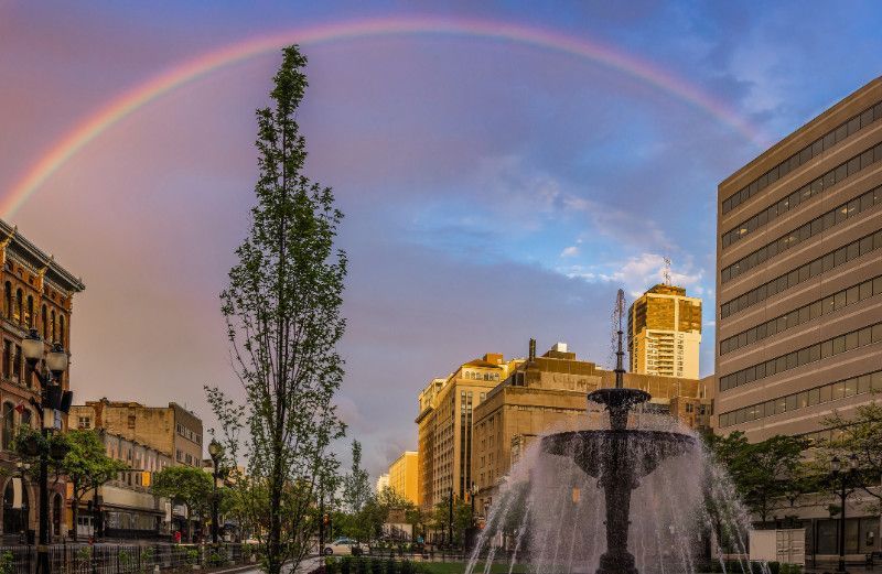 There is a rainbow over a fountain in the middle of Hamilton, Ontario